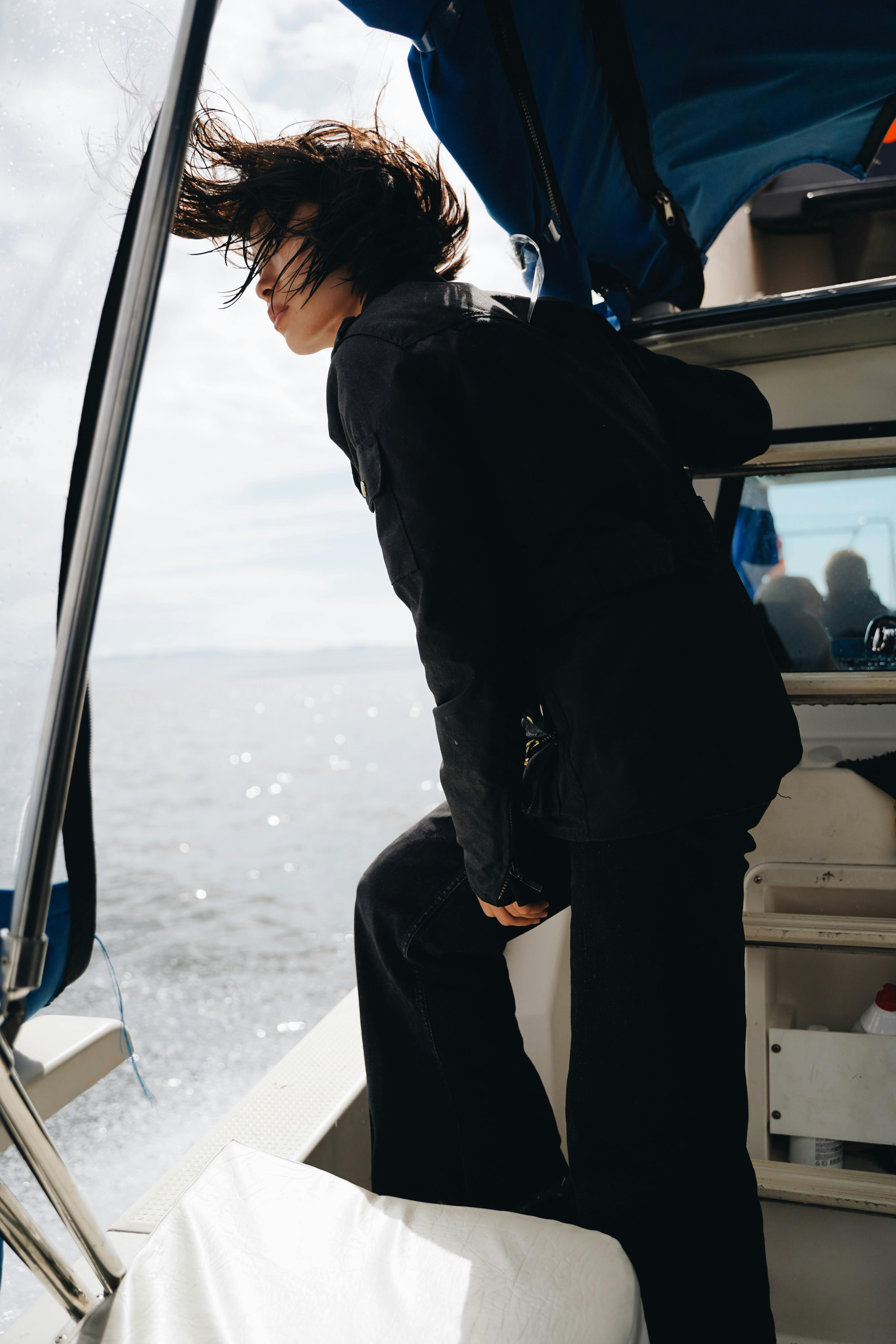 A woman in a black jacket stands on a boat, enjoying the open water scenery.