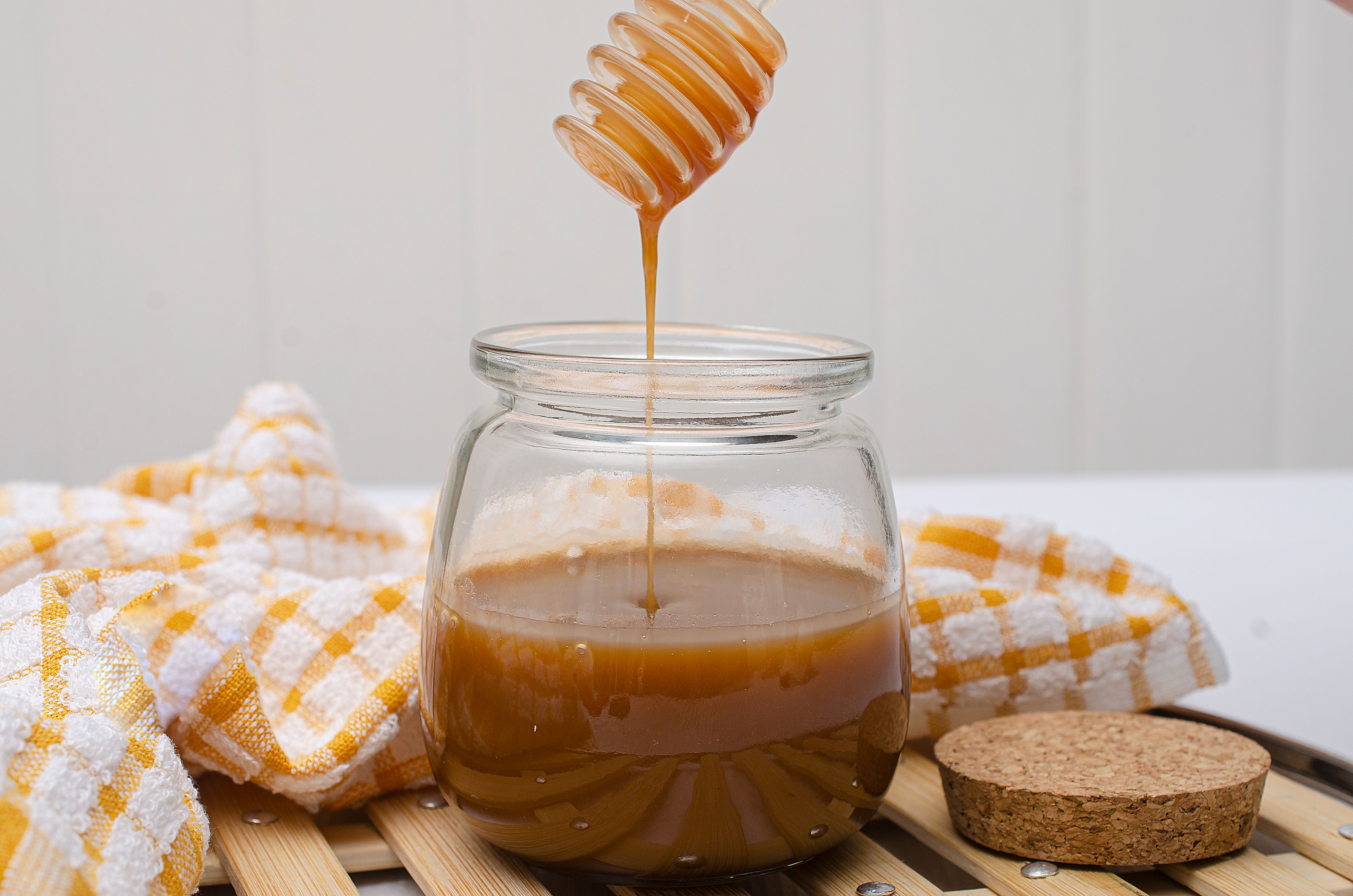 Clear glass jar of honey with a wooden dipper on a wooden surface