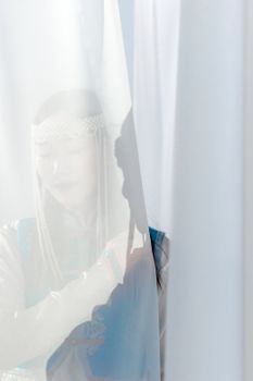 Artistic portrait of a woman partially hidden behind a sheer curtain, creating a mysterious and serene atmosphere.