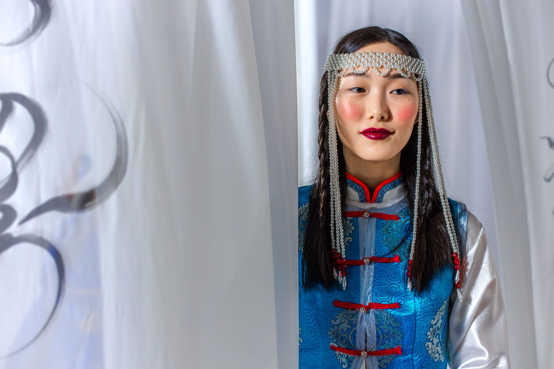 Beautiful Asian woman in traditional Mongolian attire with braided hair and pearl headpiece.