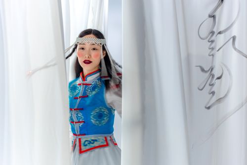 Free Asian woman in traditional Mongolian attire behind white curtains with elegant calligraphy. Stock Photo