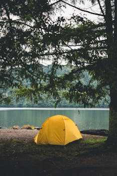 Serene lakeside camping scene featuring a bright yellow tent under trees.