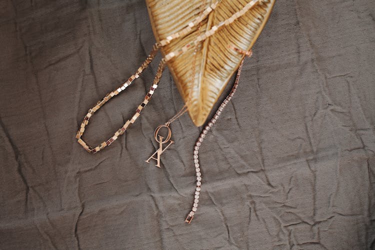 Golden Bracelet And Pendant Lying On Creased Fabric