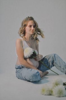 Pregnant woman in a studio, holding flowers, showcasing serenity and beauty.
