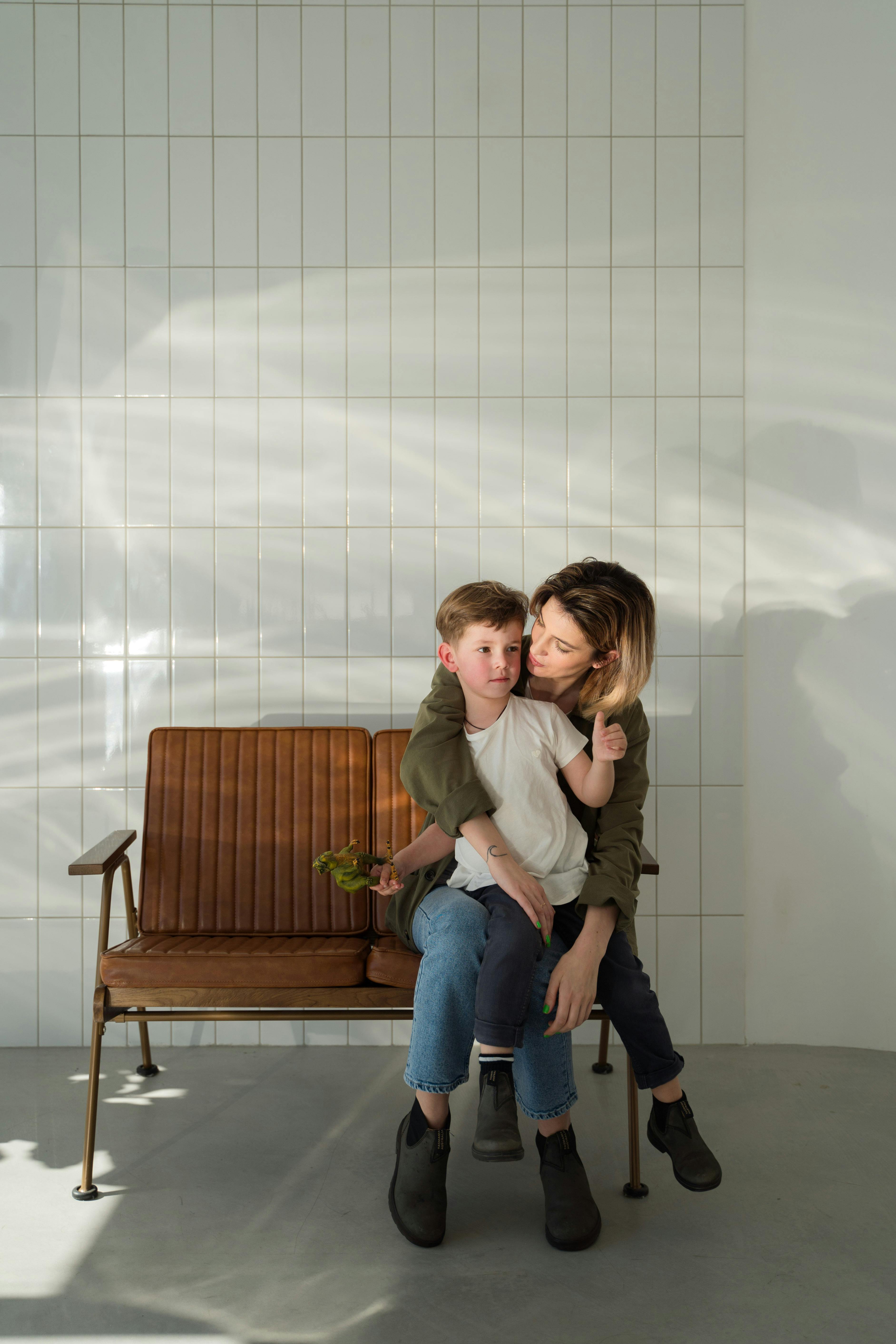A warm moment as a mother embraces her son on a wooden bench in a sunlit room.