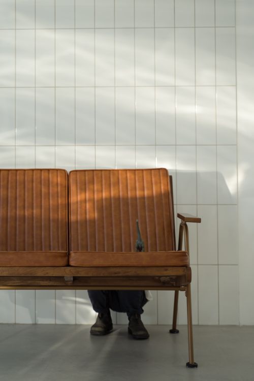 Free A playful person hides behind a brown couch with a toy dinosaur. Sunlight casts shadows on tiled wall. Stock Photo