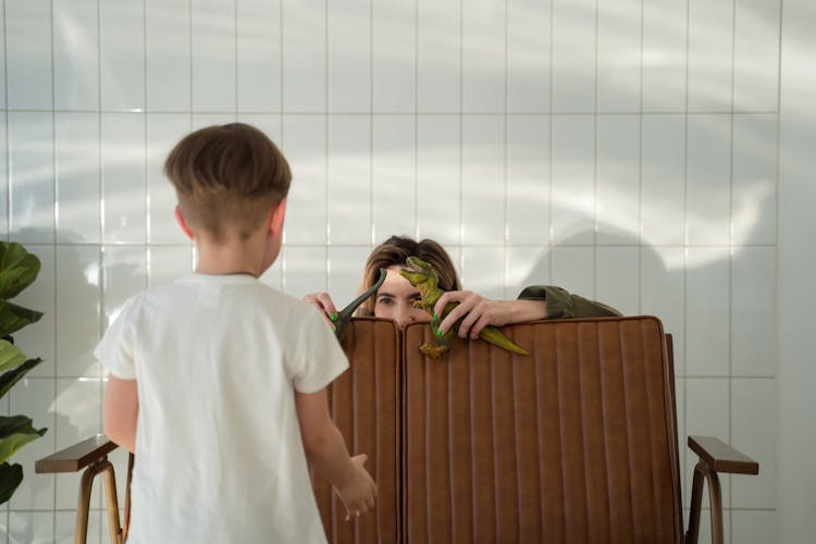 A Mother Hiding Behind The Brown Couch While Holding A Toy Dinosaur