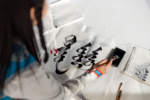 An Asian woman creates exquisite Mongolian calligraphy using black ink on paper.