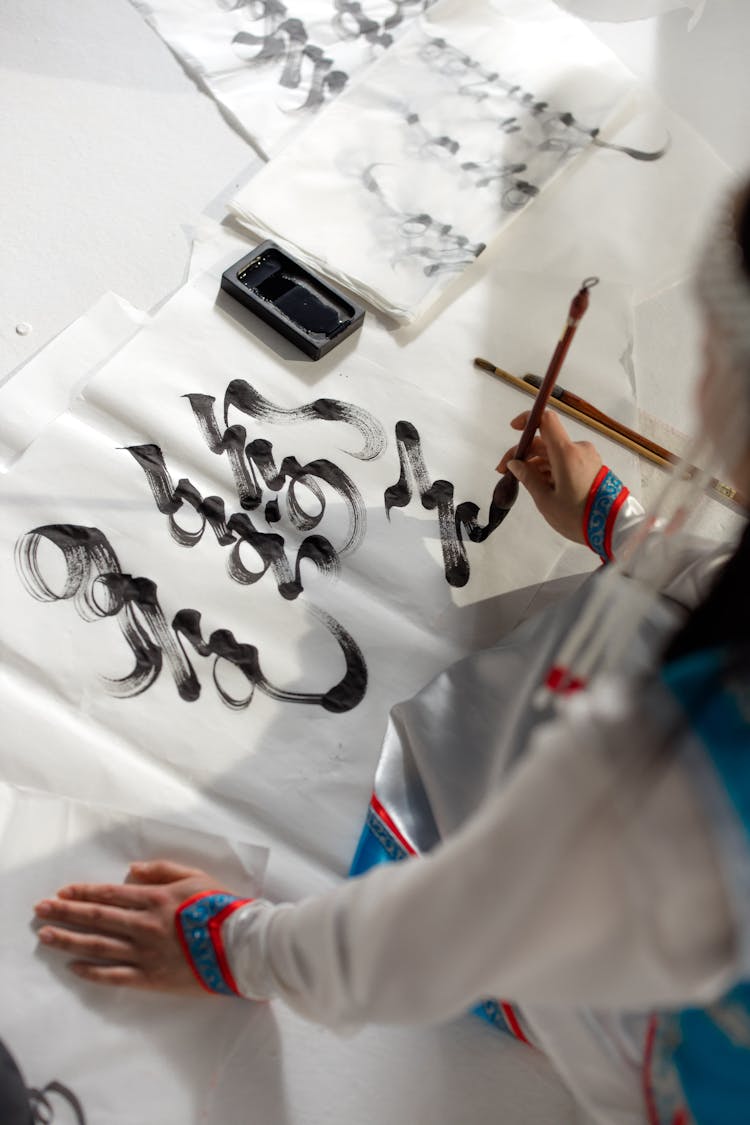 Person Holding Brush Writing On White Cloth