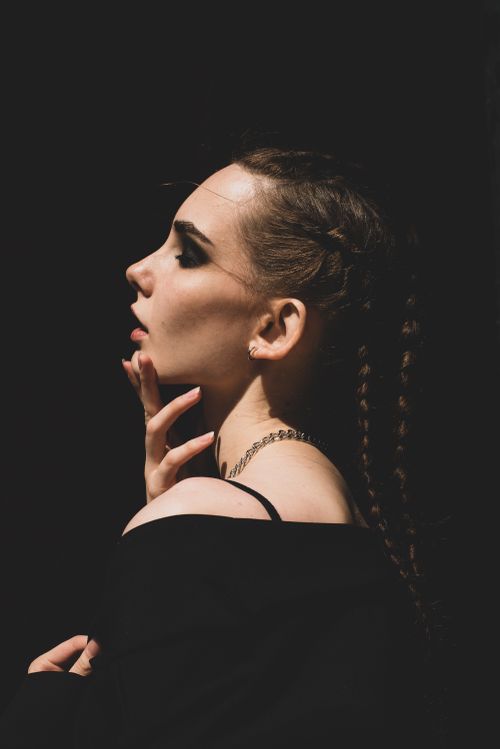Free A dramatic portrait of a stylish woman with braided hair and a black background, embodying elegance and mystery. Stock Photo