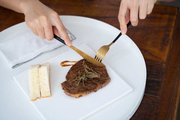 A Person Slicing A Steak On White Ceramic Plate