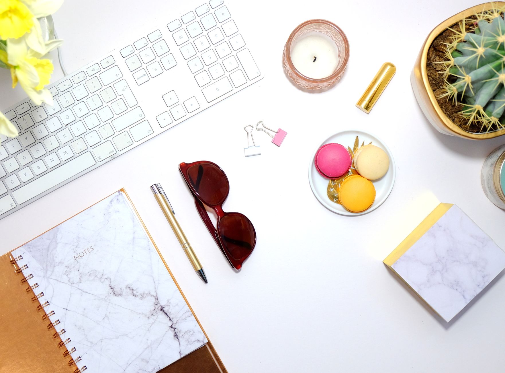 A modern flat lay of a workspace featuring macarons, cactus, and stylish accessories.