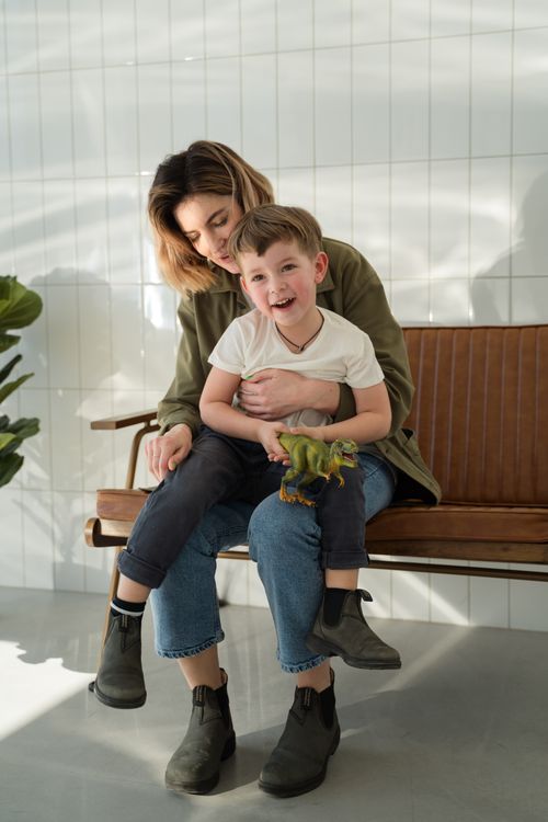 Free A mother lovingly embraces her cheerful son holding a dinosaur toy indoors. Stock Photo