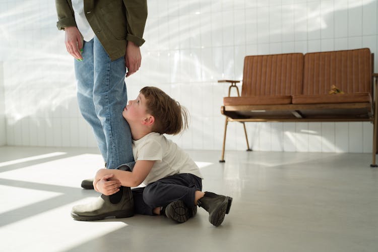 Boy Sitting On The Floor While Hugging A Person's Leg