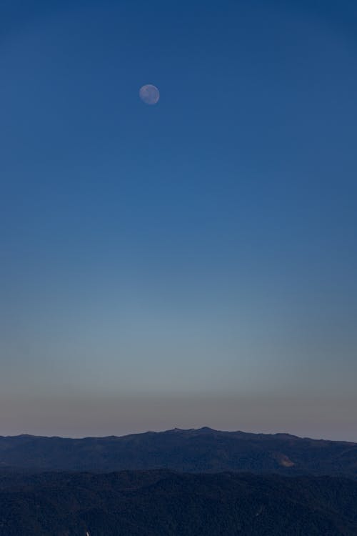 Vague Moon on Blue Sky over Mountains