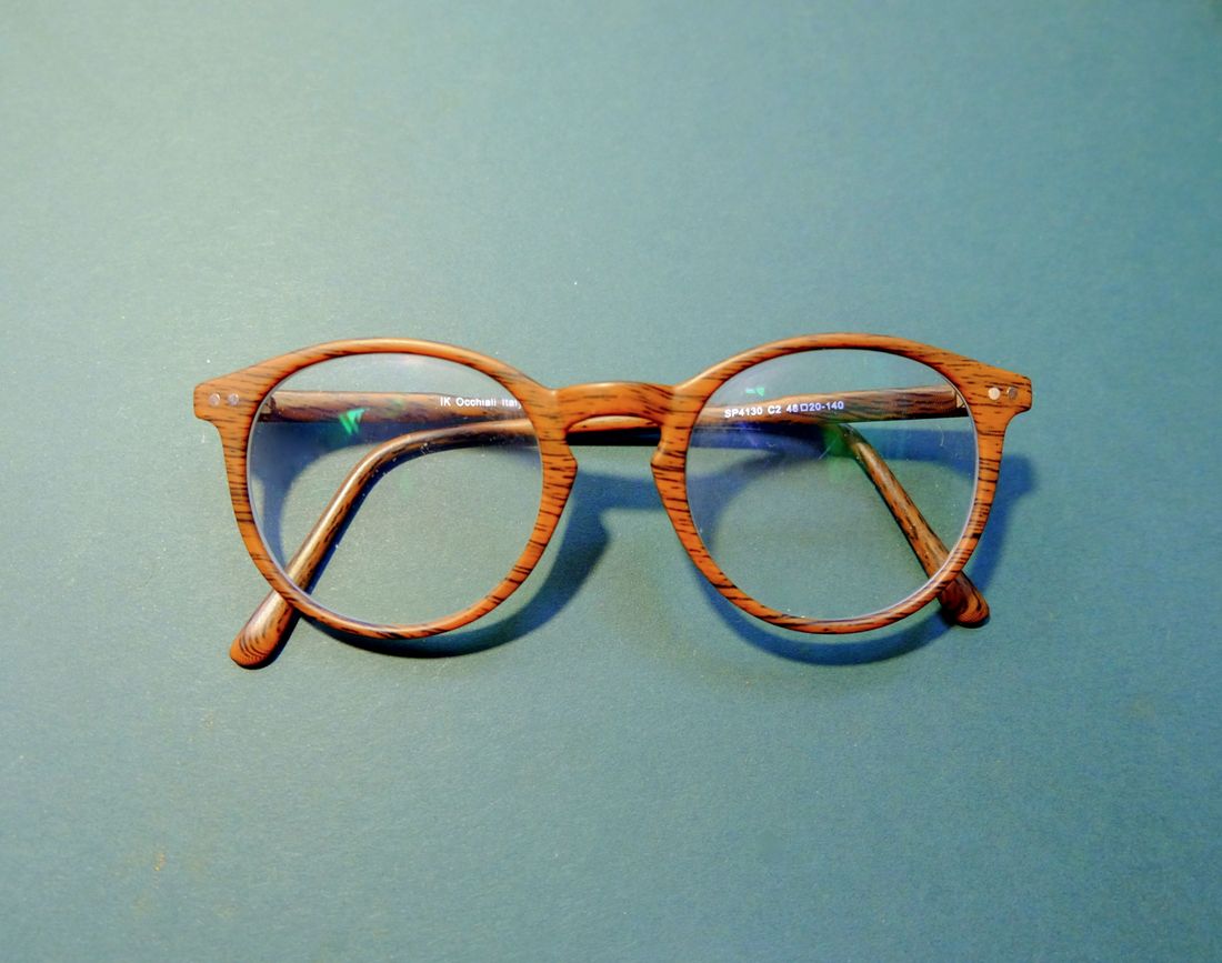 A pair of round eyeglass frames on a coloured surface