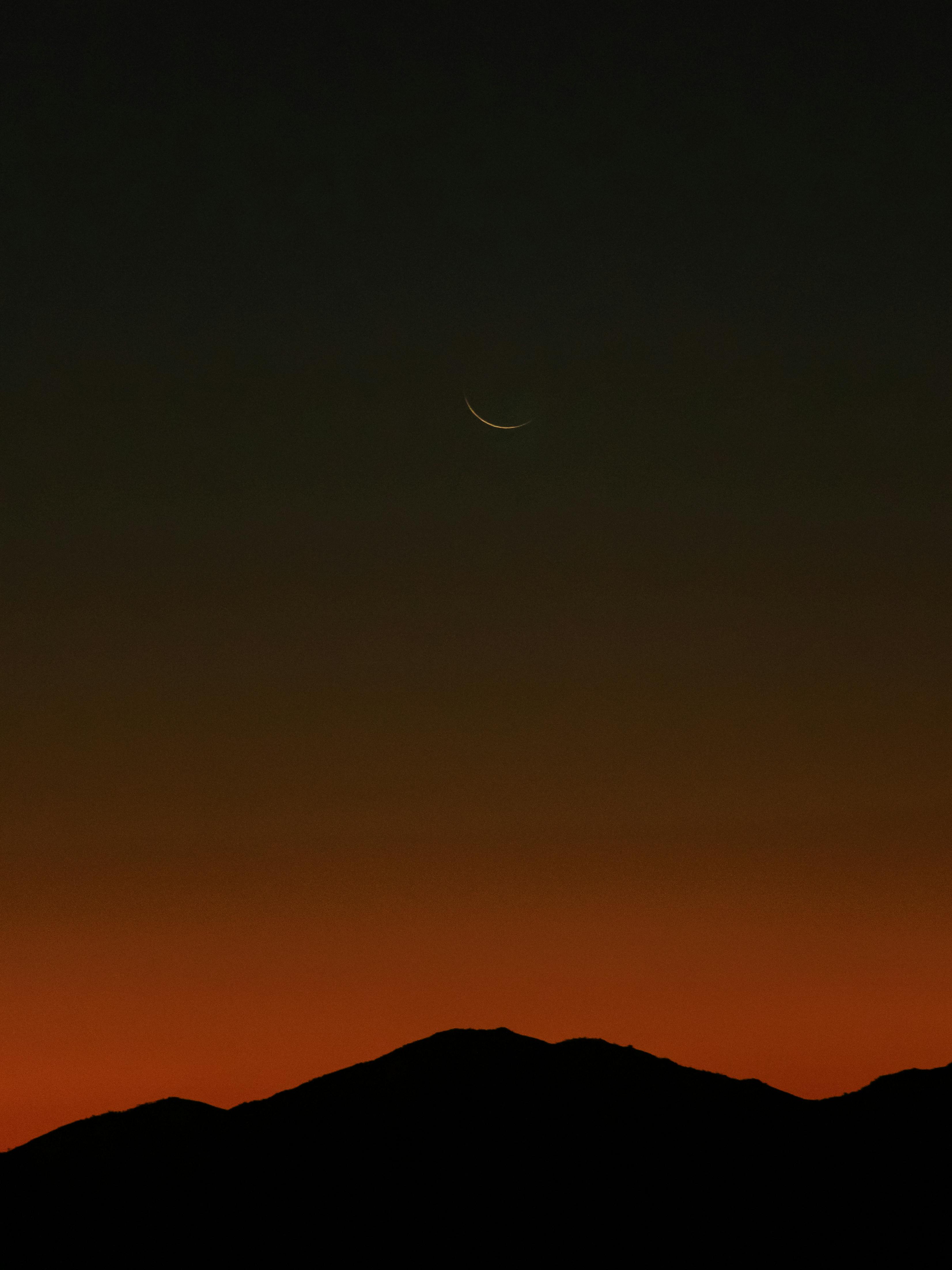 A serene twilight scene featuring a crescent moon over silhouetted mountains, perfect for backgrounds.