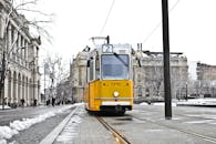 一辆黄色电车驶过白雪皑皑的布达佩斯街道，凸显了冬季公共交通的景象