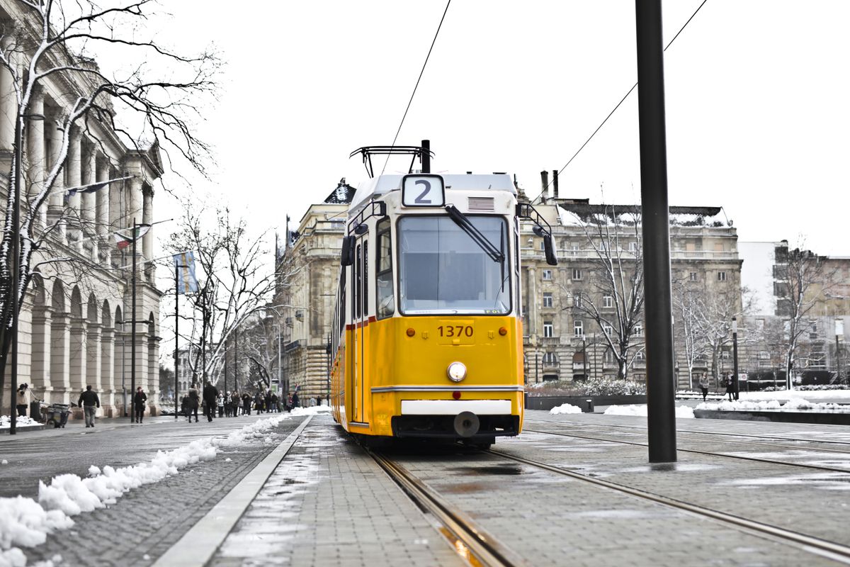 Tramvai galben trecând pe o stradă înzăpezită din Budapesta, mărginită de clădiri neoclasice