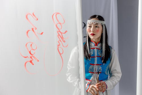 Beautiful Woman in Traditional Dress Looking at Handwritten Text on Curtain