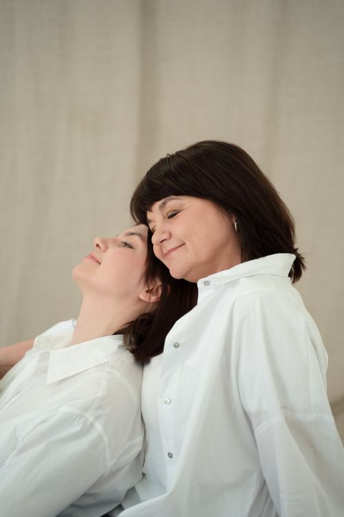 Free A heartwarming portrait of a mother and daughter wearing white shirts, sharing an affectionate gesture indoors. Stock Photo