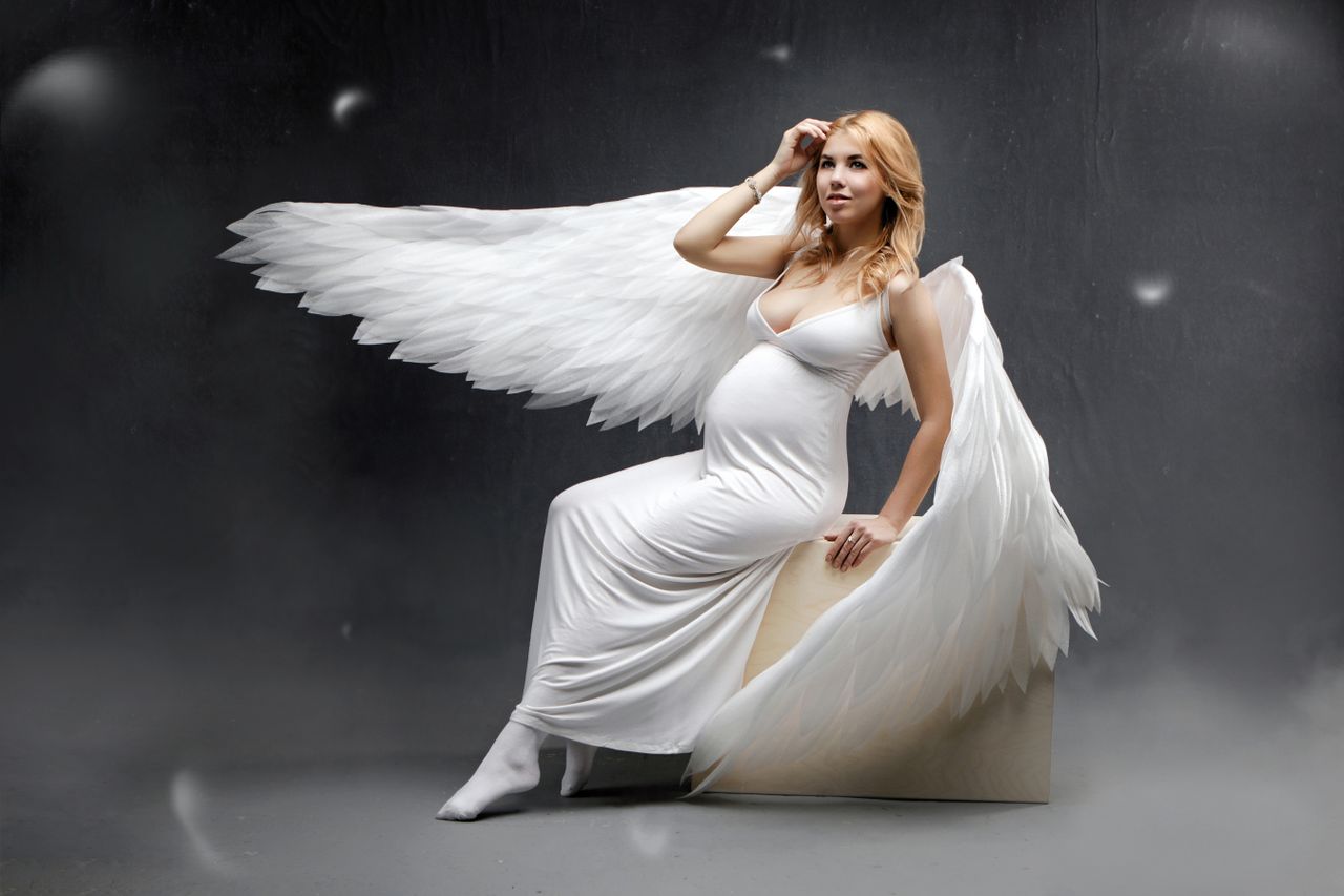 pregnant woman in an angel costume with wings seated on a cube in a st