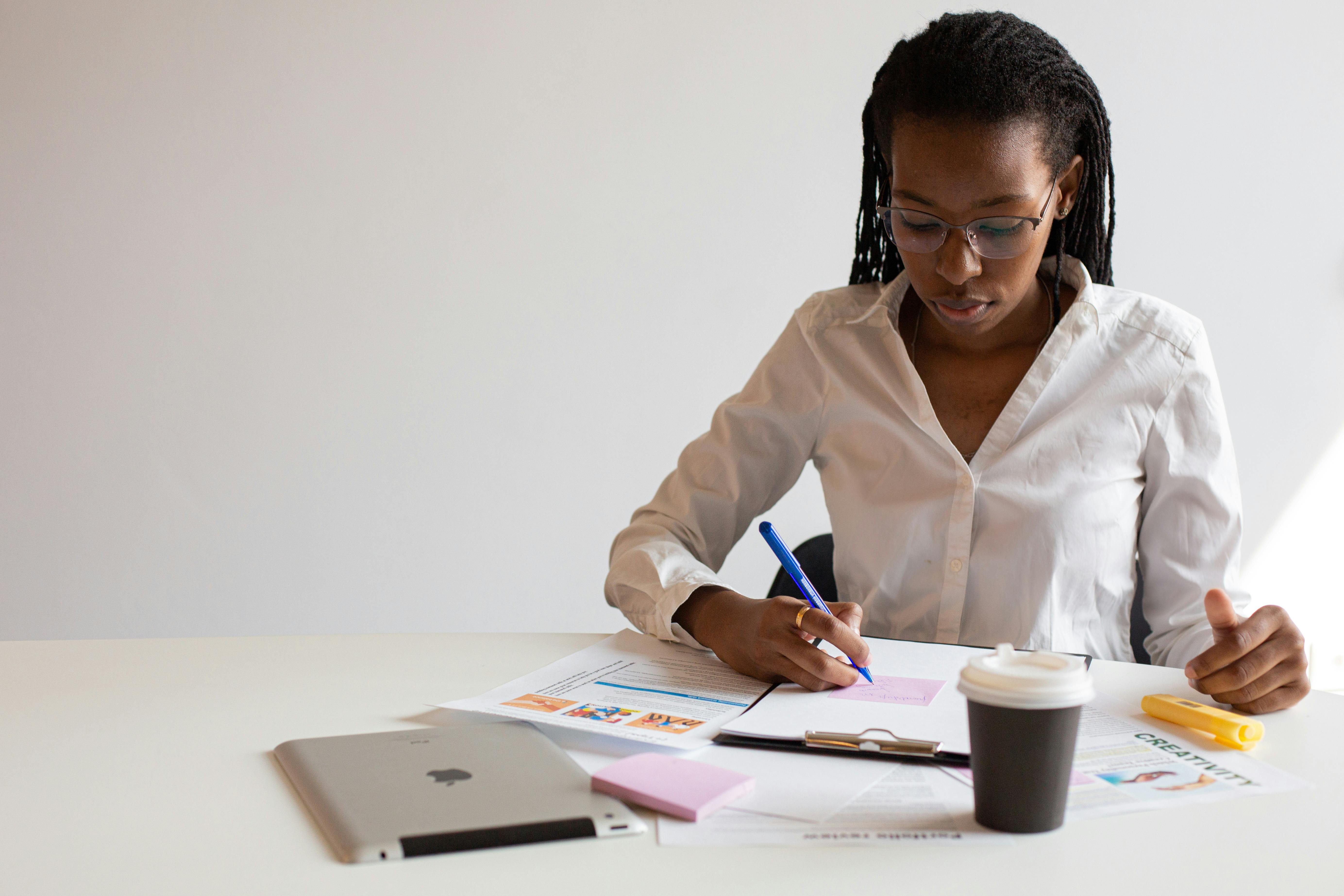 woman in white dress shirt writing down on paper