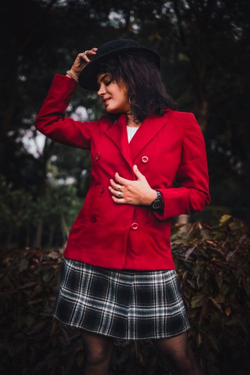 Free Young woman posing fashionably in a red blazer with a black hat in an outdoor setting. Stock Photo