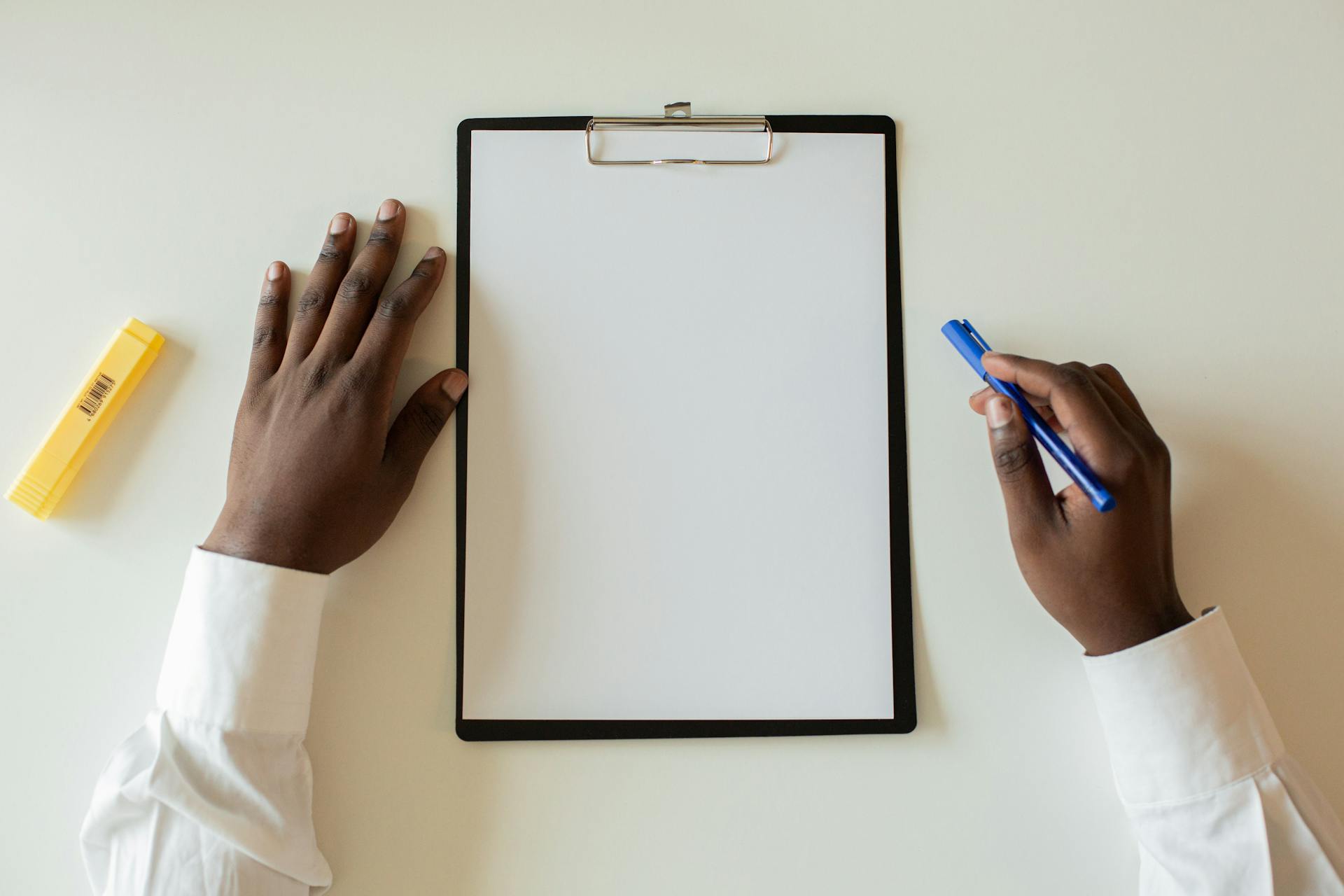 Overhead view of hands with a blank clipboard and a pen on white desk.