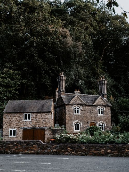 Free A picturesque brick cottage nestled among lush trees, symbolizing tranquility and rural charm. Stock Photo