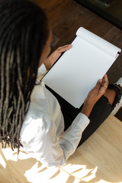 Free Overhead view of a woman sitting at a desk holding a blank clipboard, wearing ripped jeans. Stock Photo