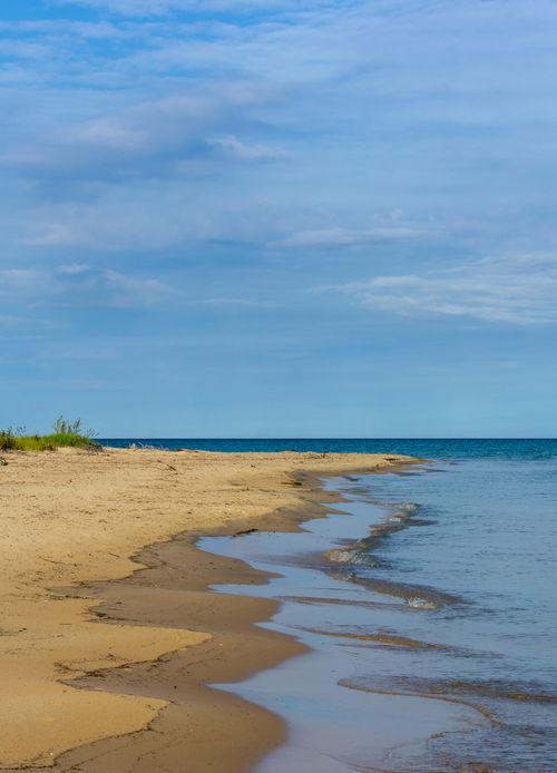 Free Tranquil sandy beach with calm waves and a clear blue sky, perfect for relaxation. Stock Photo