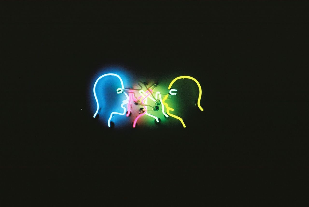 colorful neon light art installation depicting faces on a dark backgro