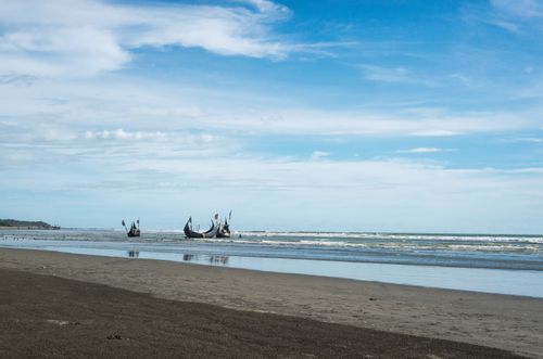 Free Serene beach view with traditional fishing boats against a clear blue sky and calm sea. Stock Photo