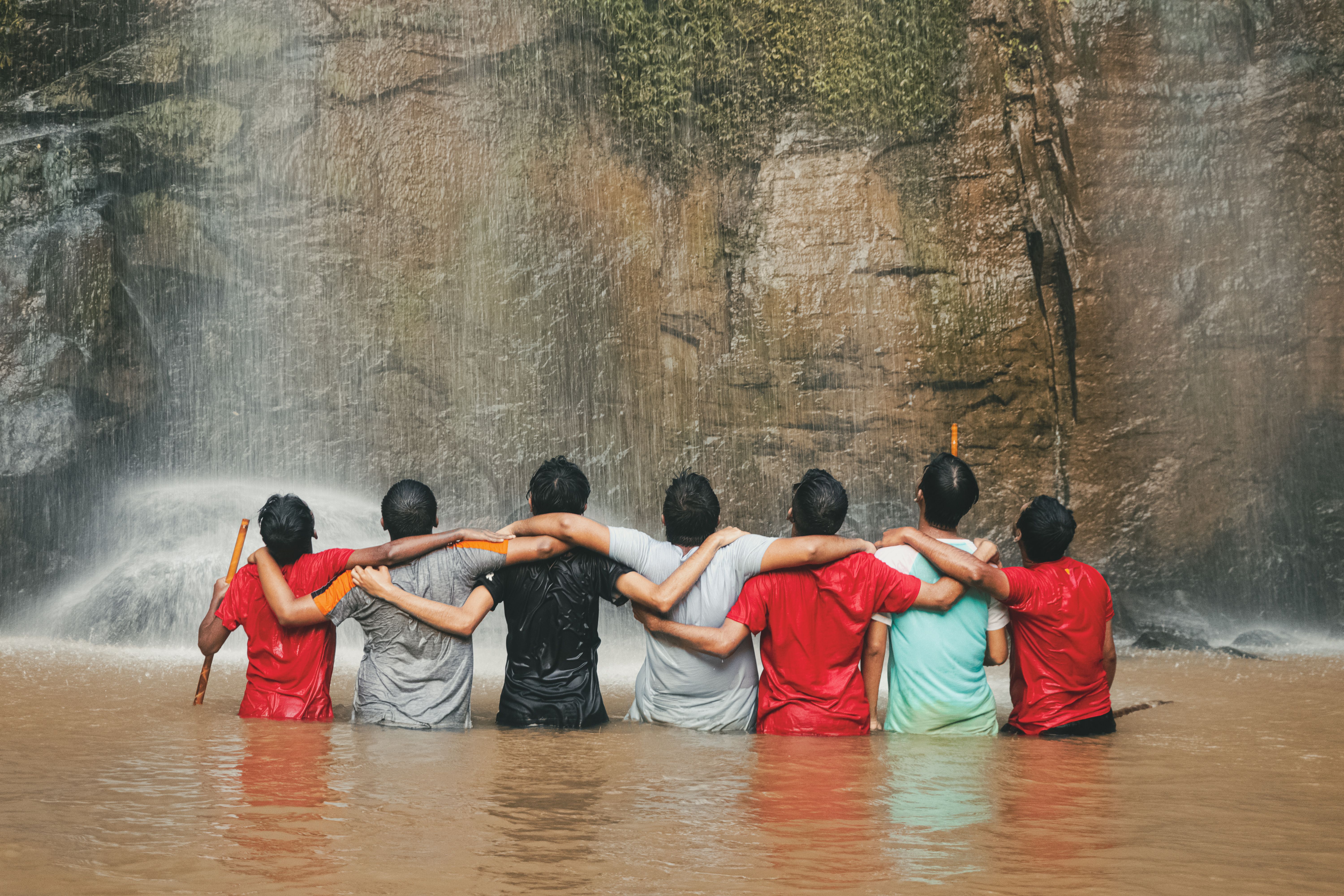 Group of people standing under a waterfall with arms raised