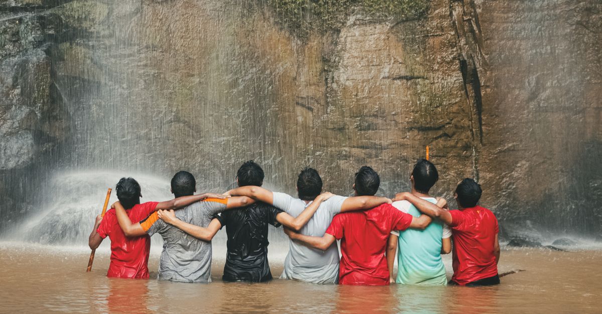 Group of people standing under a waterfall with arms raised