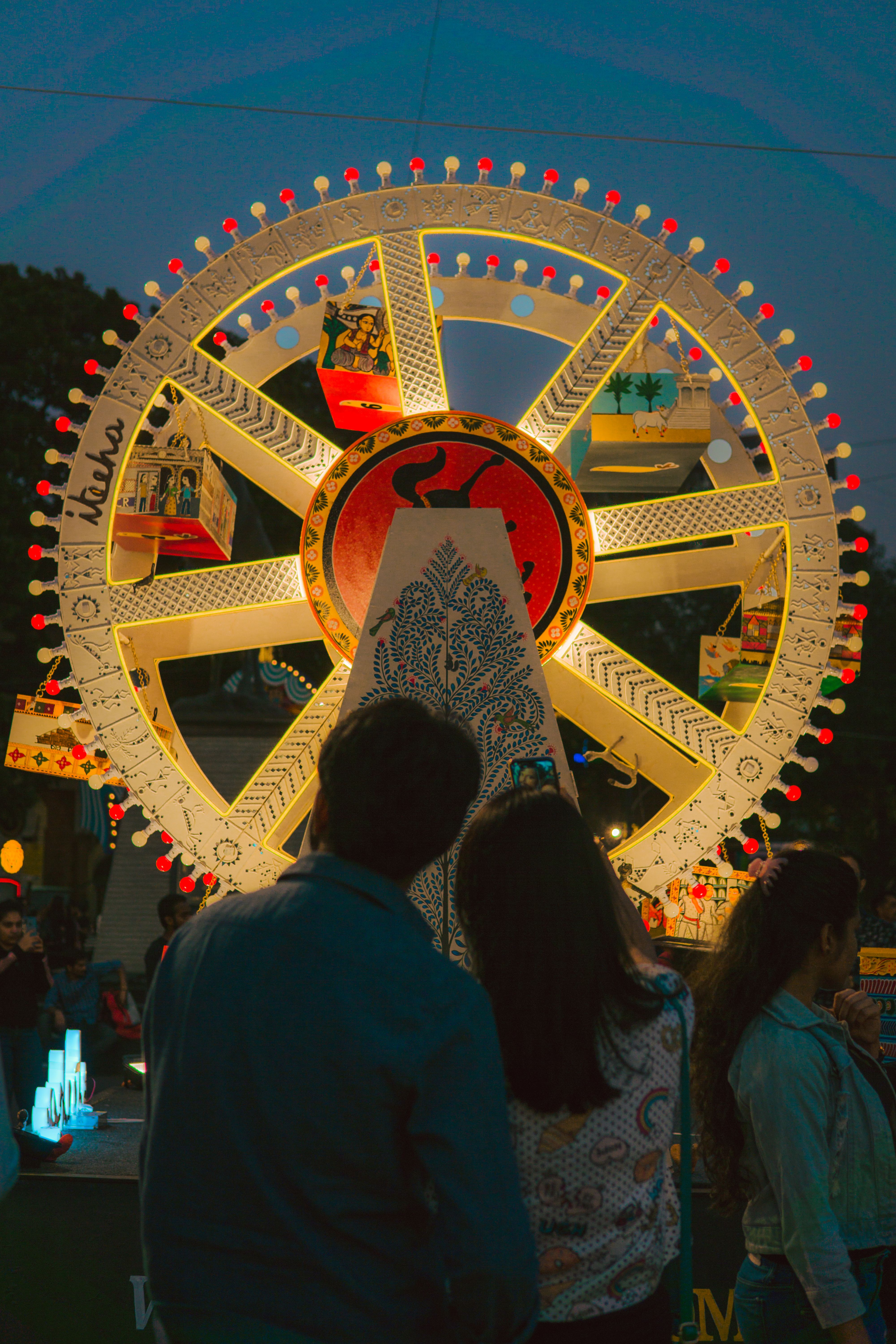 People enjoying a vibrant Ferris wheel illuminated at night in a carnival setting.
