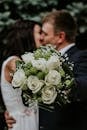 一对夫妇手捧白玫瑰和绿色花卉的婚礼花束相拥
