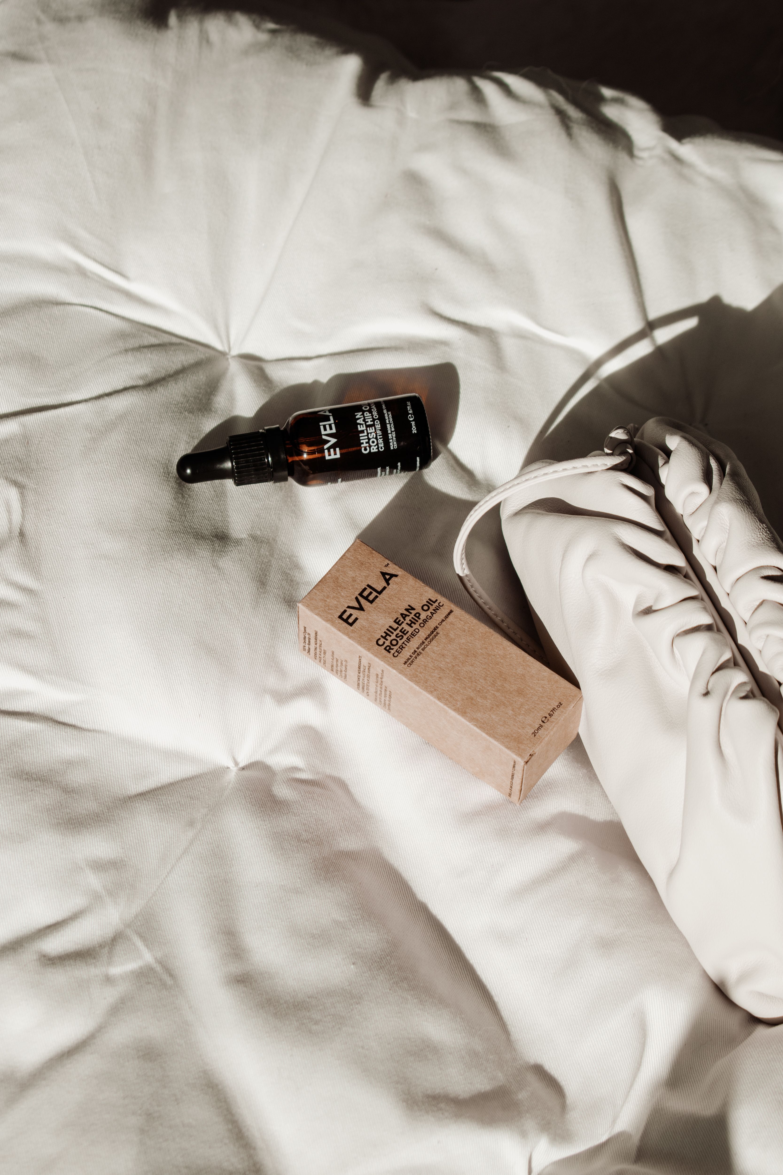 Flat lay of rose hip oil bottle and packaging on white fabric, with bag. Ideal for beauty concepts.