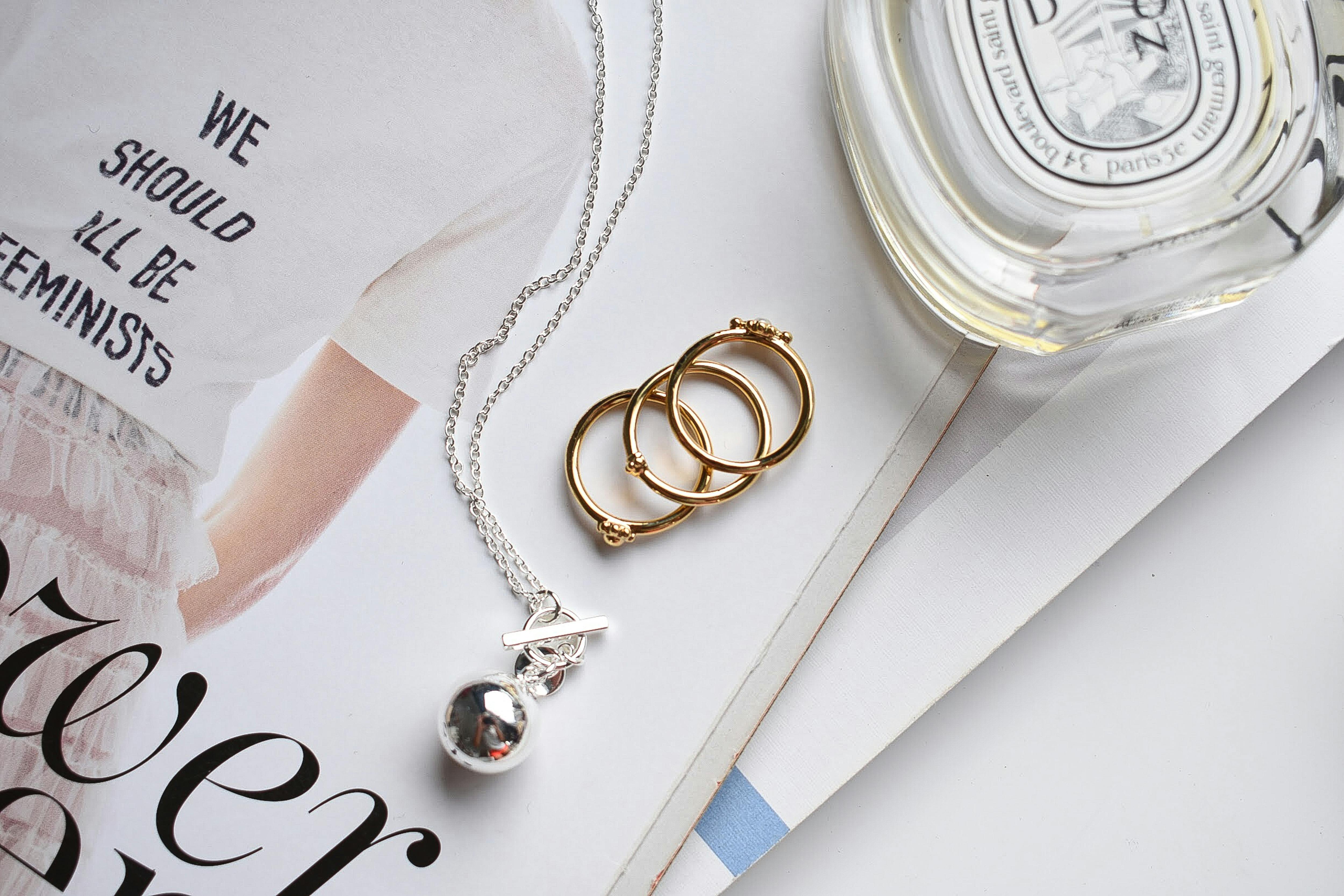 Editorial flat lay of fine jewelry in mixed metals — silver and gold pendants, rings, and earrings arranged on a neutral surface