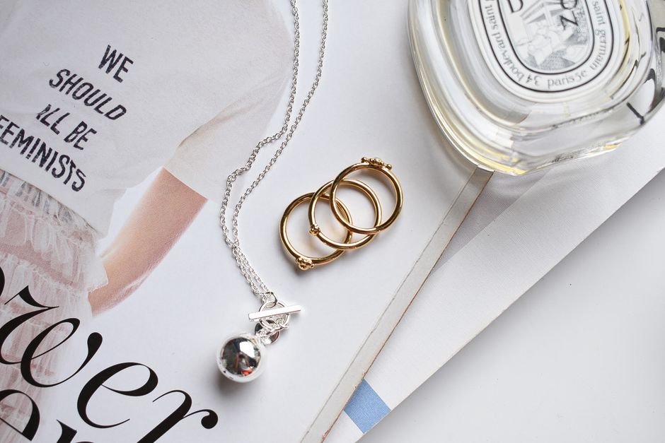 Editorial flat lay of fine jewelry in mixed metals — silver and gold pendants, rings, and earrings arranged on a neutral surface