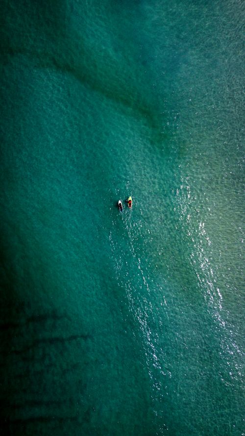 Free Drone shot capturing two paddleboarders enjoying the clear green waters of Brazil. Stock Photo