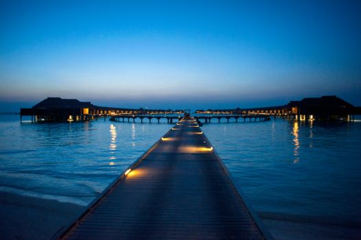 Peaceful view of overwater bungalows at twilight with a wooden dock leading to them.