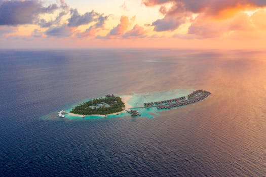 Photo by Asad Photo Maldives A picturesque aerial view of a tropical island resort surrounded by clear blue ocean during a vibrant sunset.