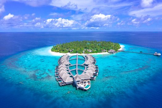 Stunning aerial shot of a resort on a tropical island in the Maldives, surrounded by turquoise waters.