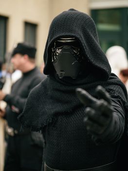 A person in detailed black cosplay outfit with helmet and mask pointing forward.