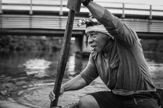 Black and white photo of an elderly fisherman paddling a rowboat in Colón, Panama.