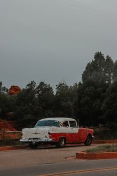 A classic red and white vintage car parked on a scenic road in Colorado Springs.
