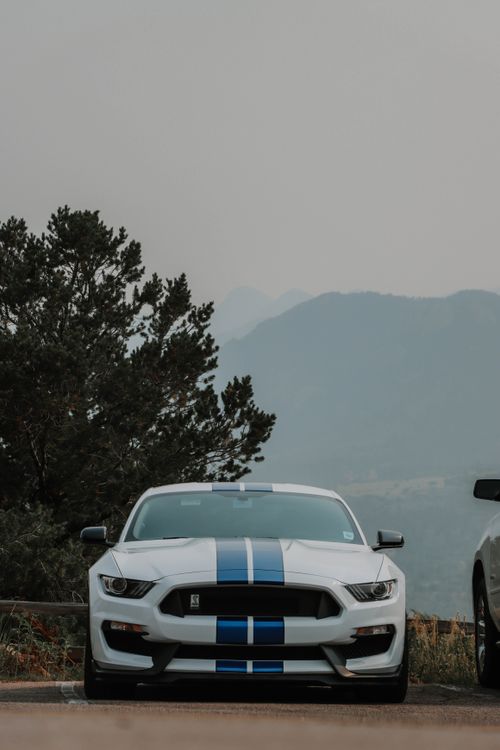 Free Front view of a white Ford Mustang with blue stripes, set against a Colorado Springs mountain backdrop. Stock Photo