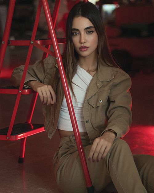 Free A fashionable woman poses confidently indoors, using a red stepladder for an artistic touch. Stock Photo